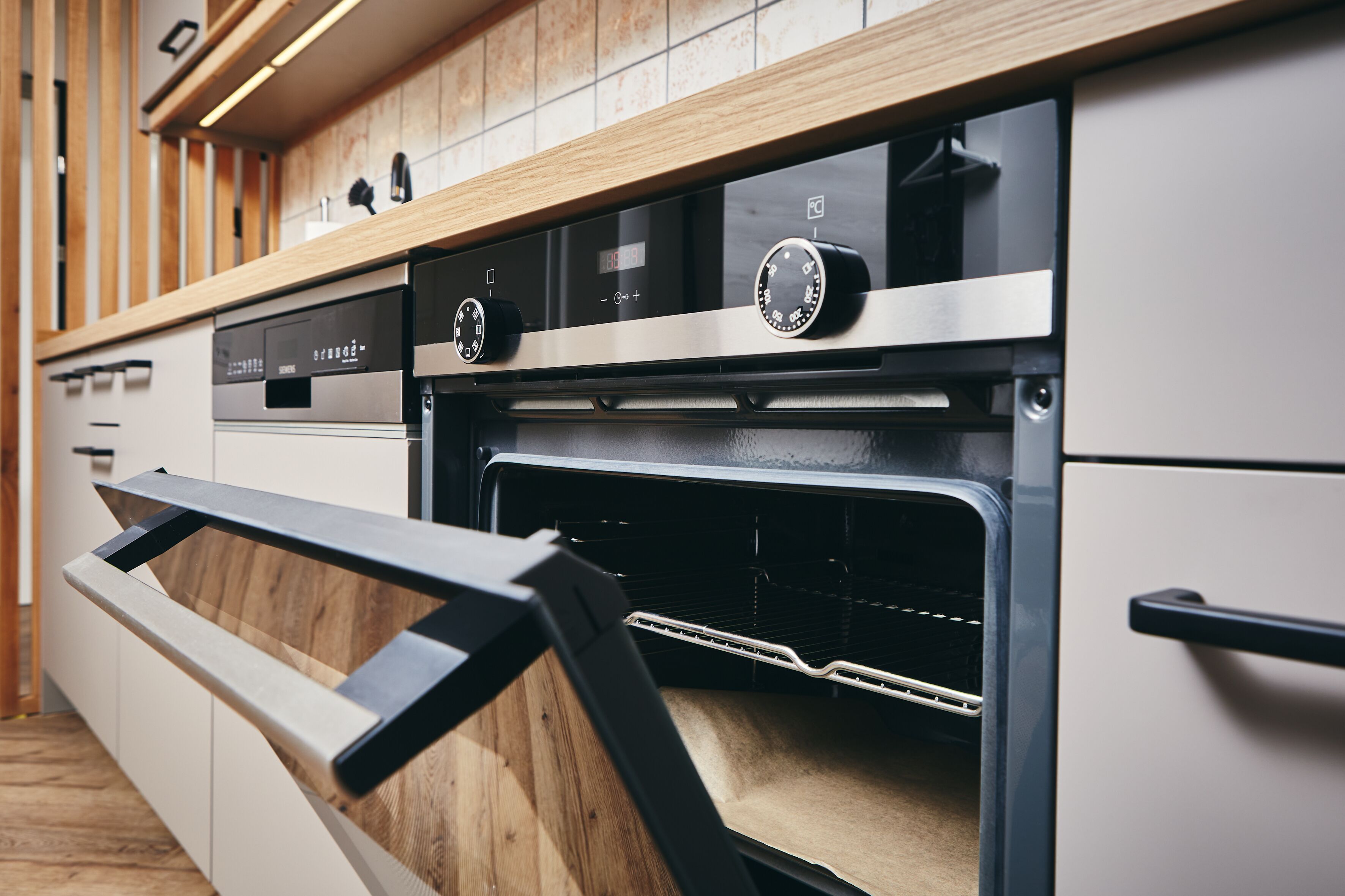 A modern kitchen with a built-in oven, wooden cabinetry, and stainless steel appliances.