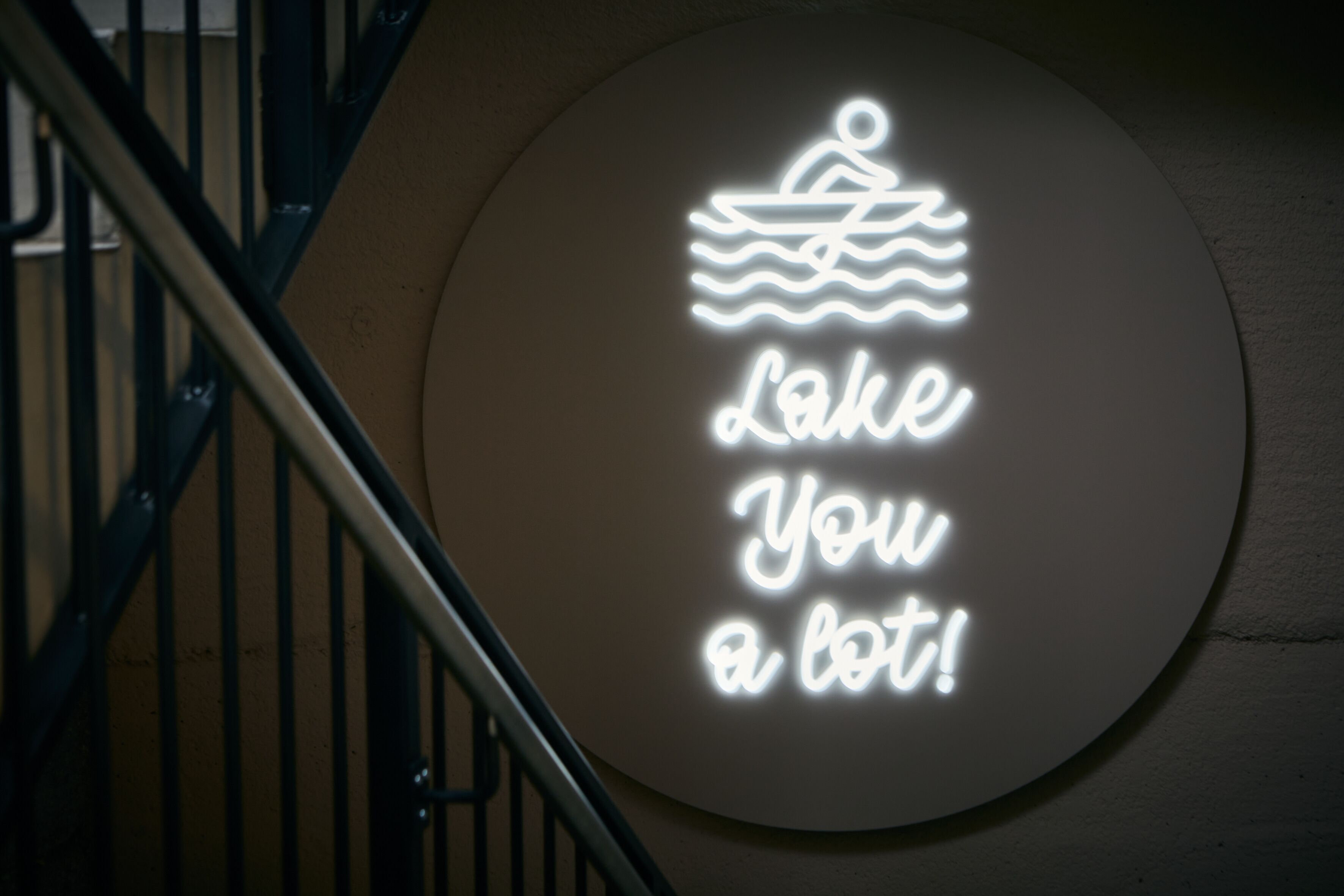 A circular sign with a neon light design featuring a person in a boat and the text 'Lake You a lot!'