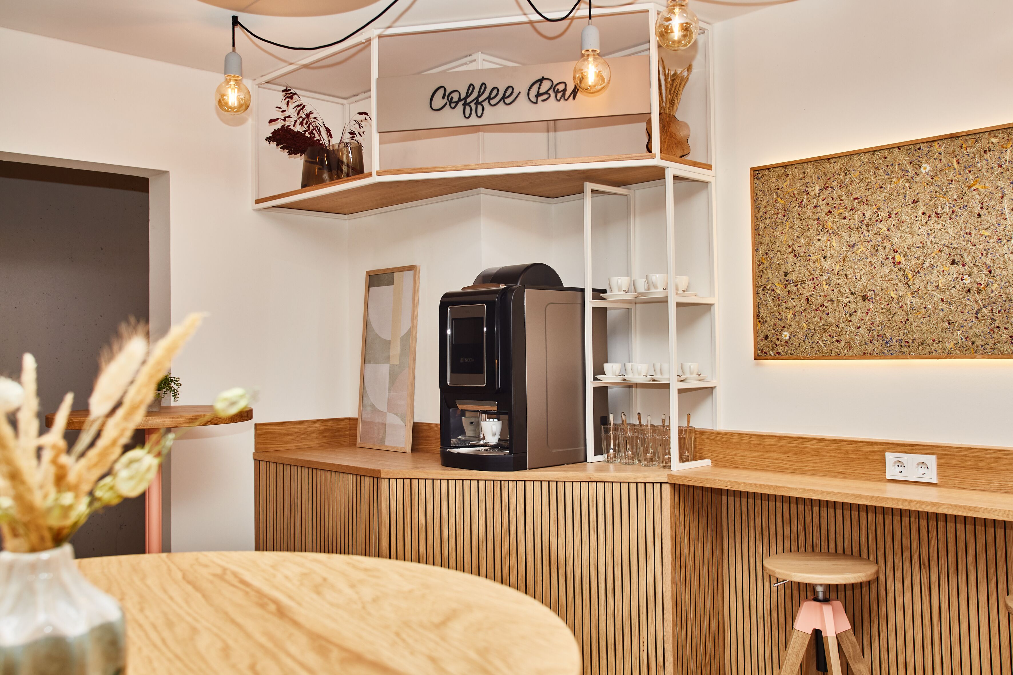 A coffee bar with a coffee machine, shelves with cups and glasses, and a wooden counter.