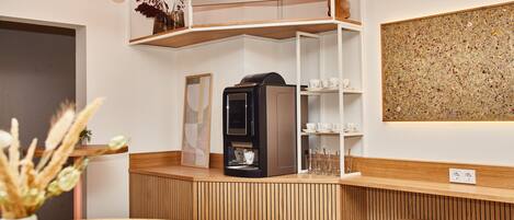 A coffee bar with a coffee machine, shelves with cups and glasses, and a wooden counter.