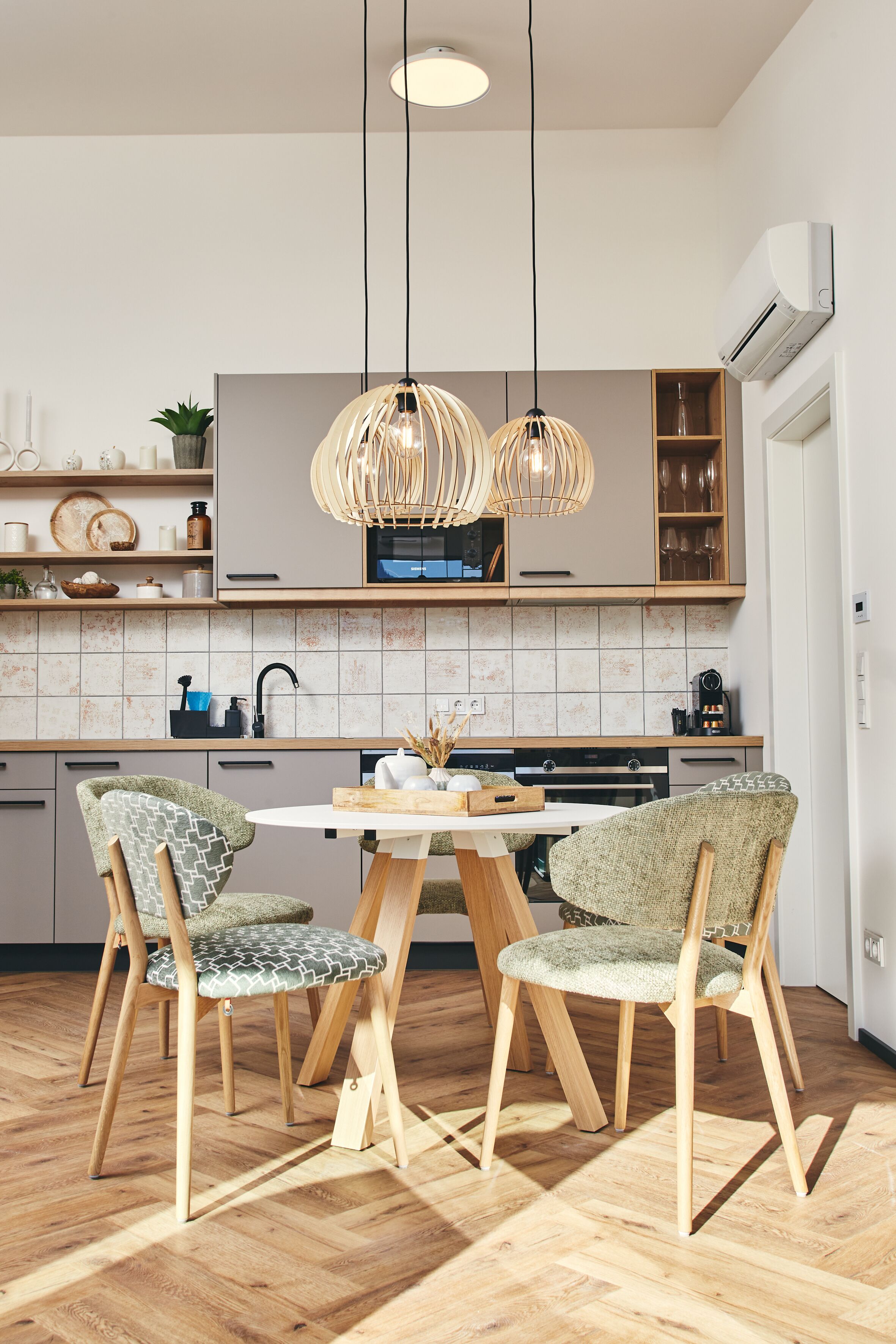 Una cocina moderna con armarios de madera, una isla central, iluminación colgante y un comedor con sillas estampadas.
