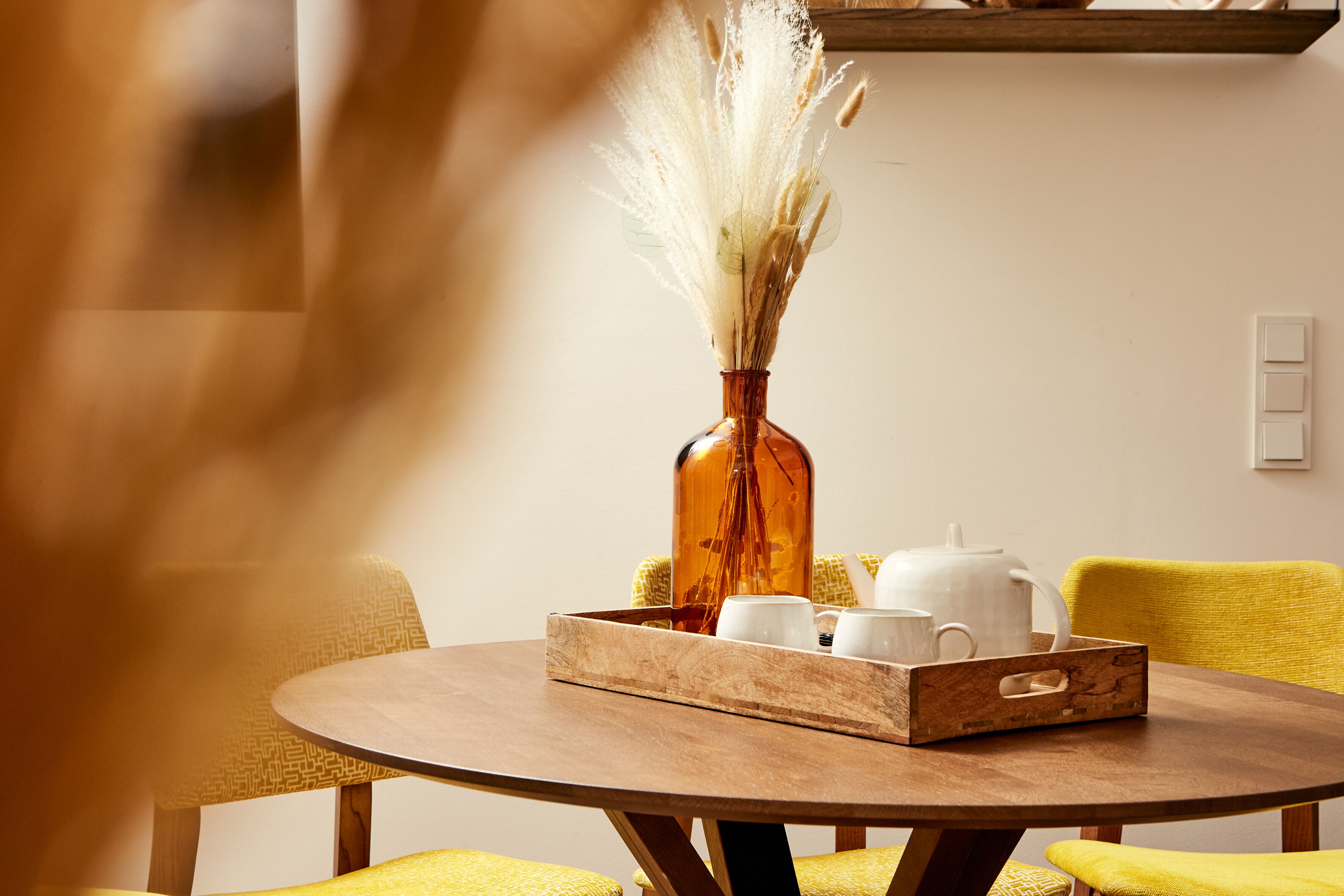 A round wooden table with a tray holding white cups and a teapot, set on a yellow chair.