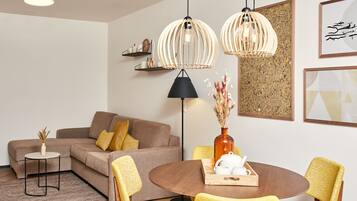 A modern living room with a brown sofa, yellow chairs, a round dining table, and two pendant lights.