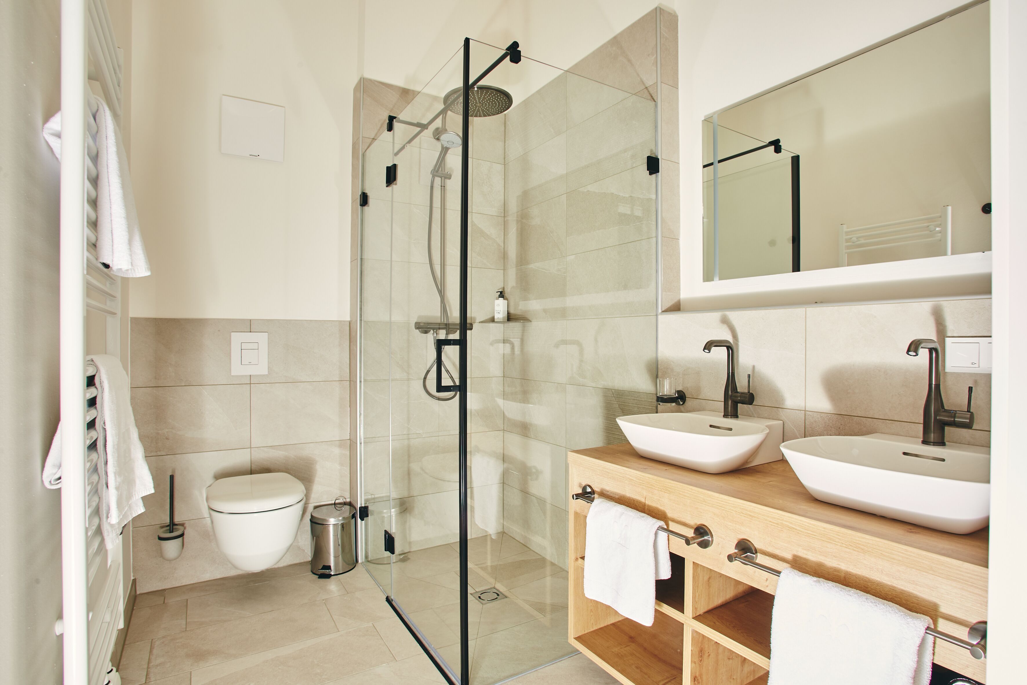 A modern bathroom with a glass-enclosed shower, two sinks, a toilet, and a mirror above the sink.