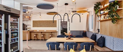 A modern restaurant with a wooden bar, blue upholstered seating, and a variety of hanging light fixtures.