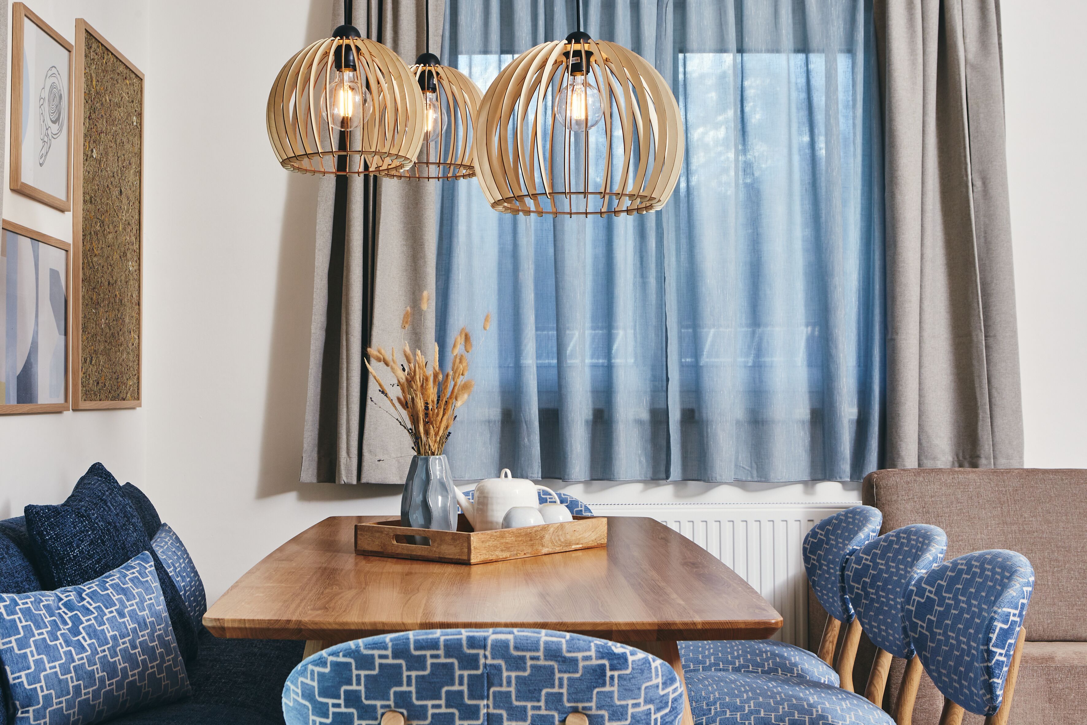 Un salon moderne avec une table à manger en bois, des chaises à motifs bleus et un canapé. Deux lampes suspendues en bois sont fixées au-dessus de la table.