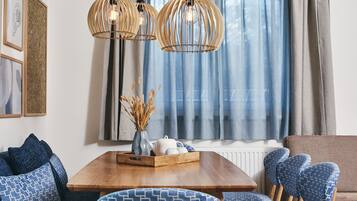 A modern living room with a wooden dining table, blue patterned chairs, and a sofa. There are two wooden pendant lights above the table.