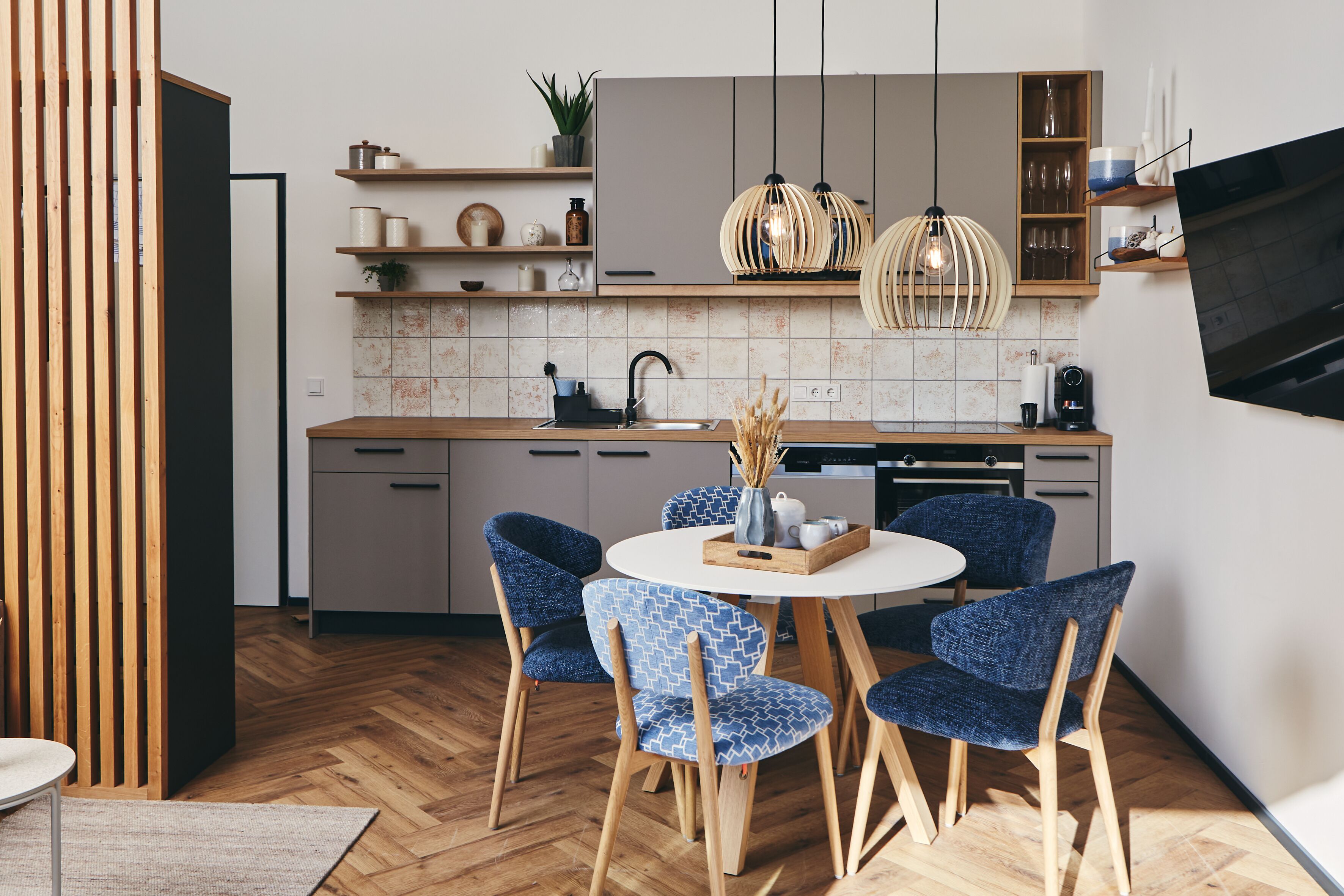 A modern kitchen with wooden cabinets, a central island, and blue patterned chairs.
