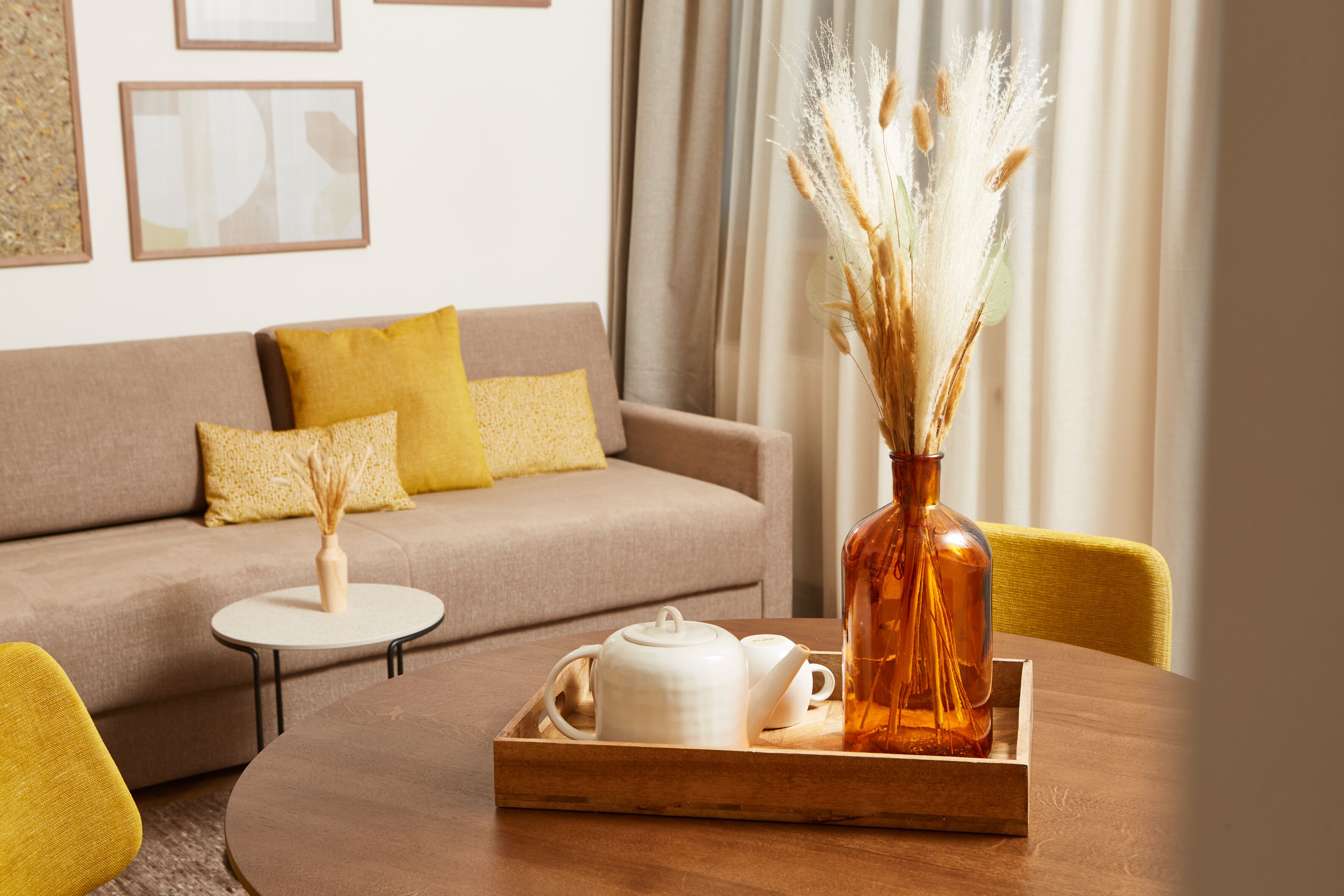 A cozy living room with a sofa, a coffee table, and a tray with a teapot and a vase with dried plants.