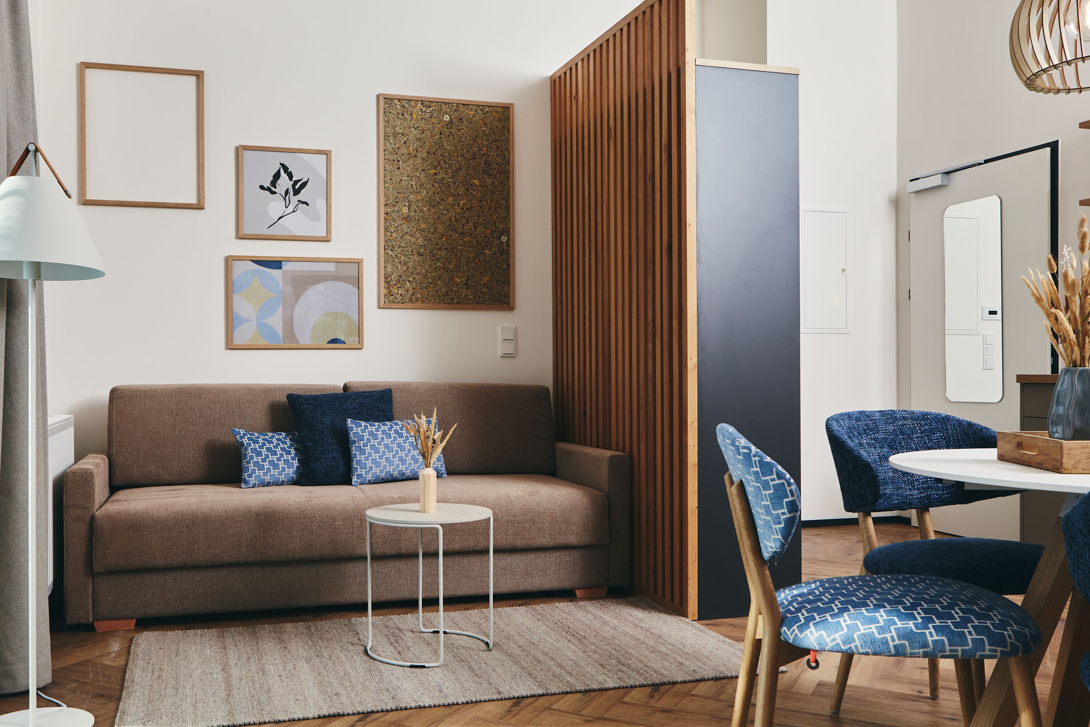 Uma sala de estar moderna com um sofá castanho, cadeiras azuis estampadas, uma mesa redonda pequena e obras de arte na parede.
