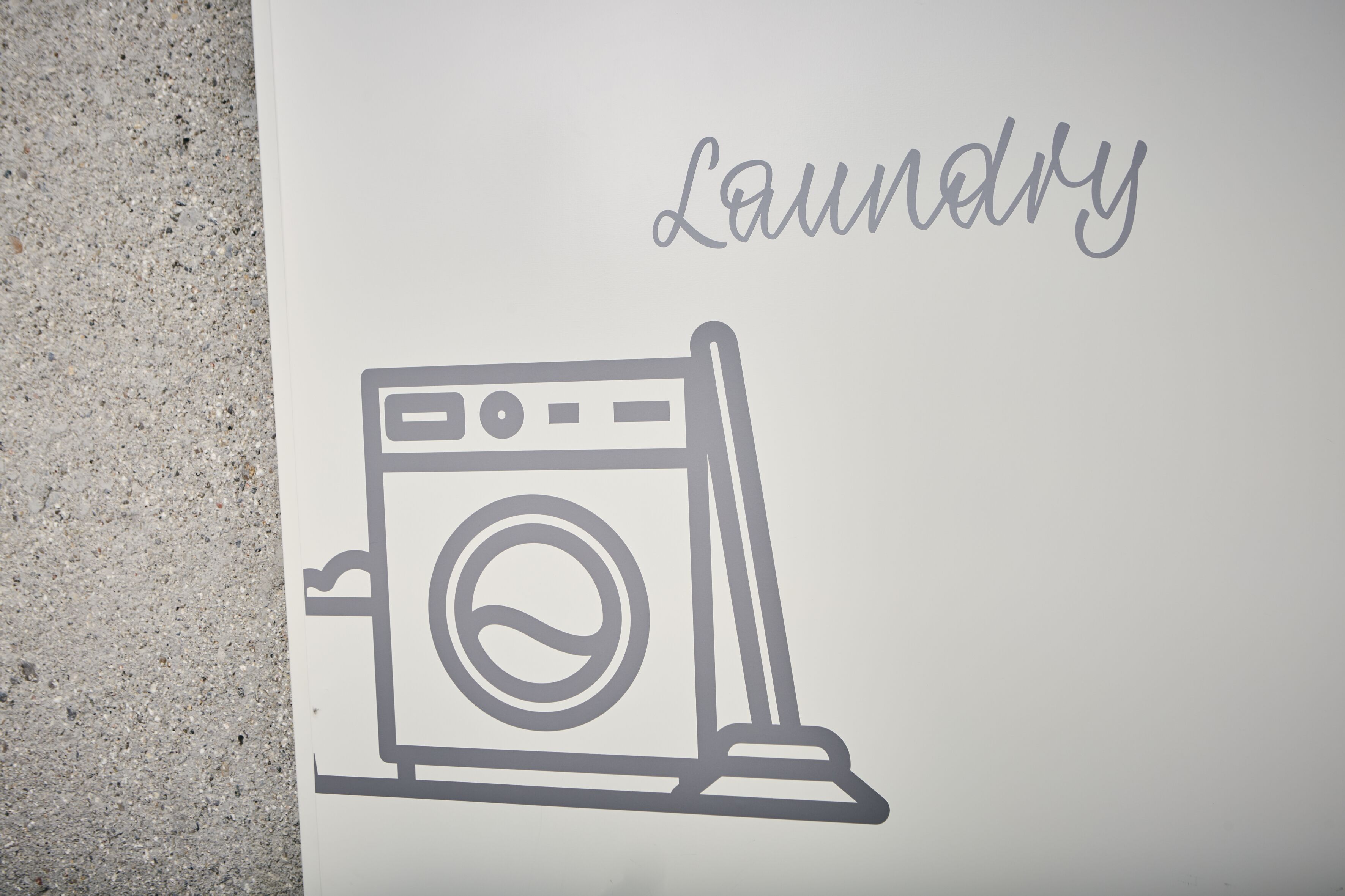 Un panneau blanc avec un symbole représentant une laverie et le mot « Laverie » écrit en lettres cursives.