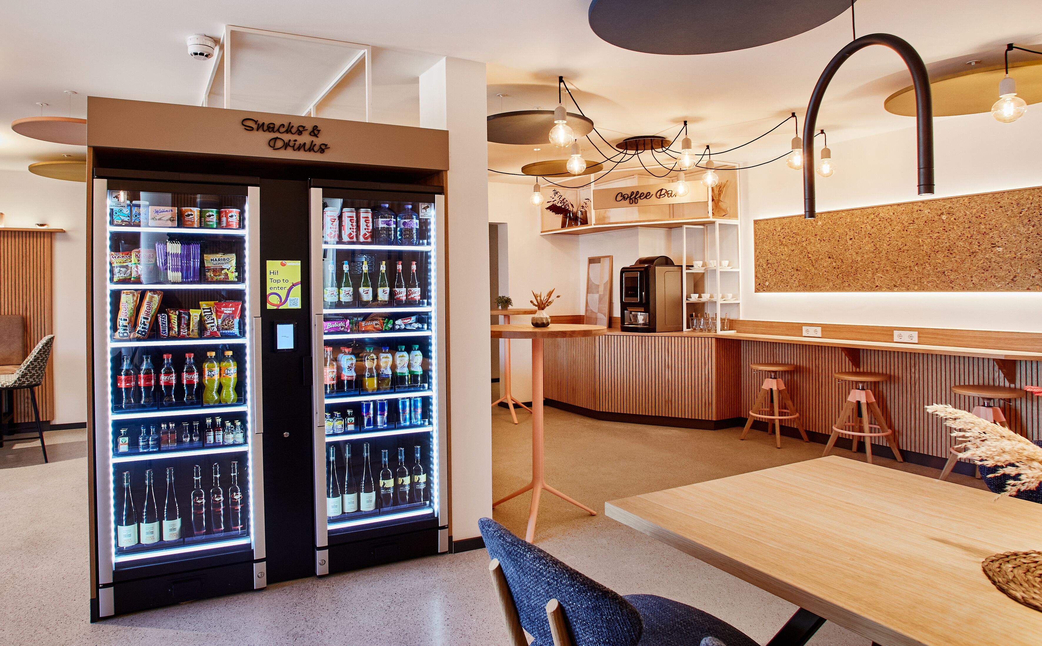 Un café équipé d’un distributeur automatique de boissons et d’en-cas, d’un comptoir à café et d’une table en bois avec des tabourets.