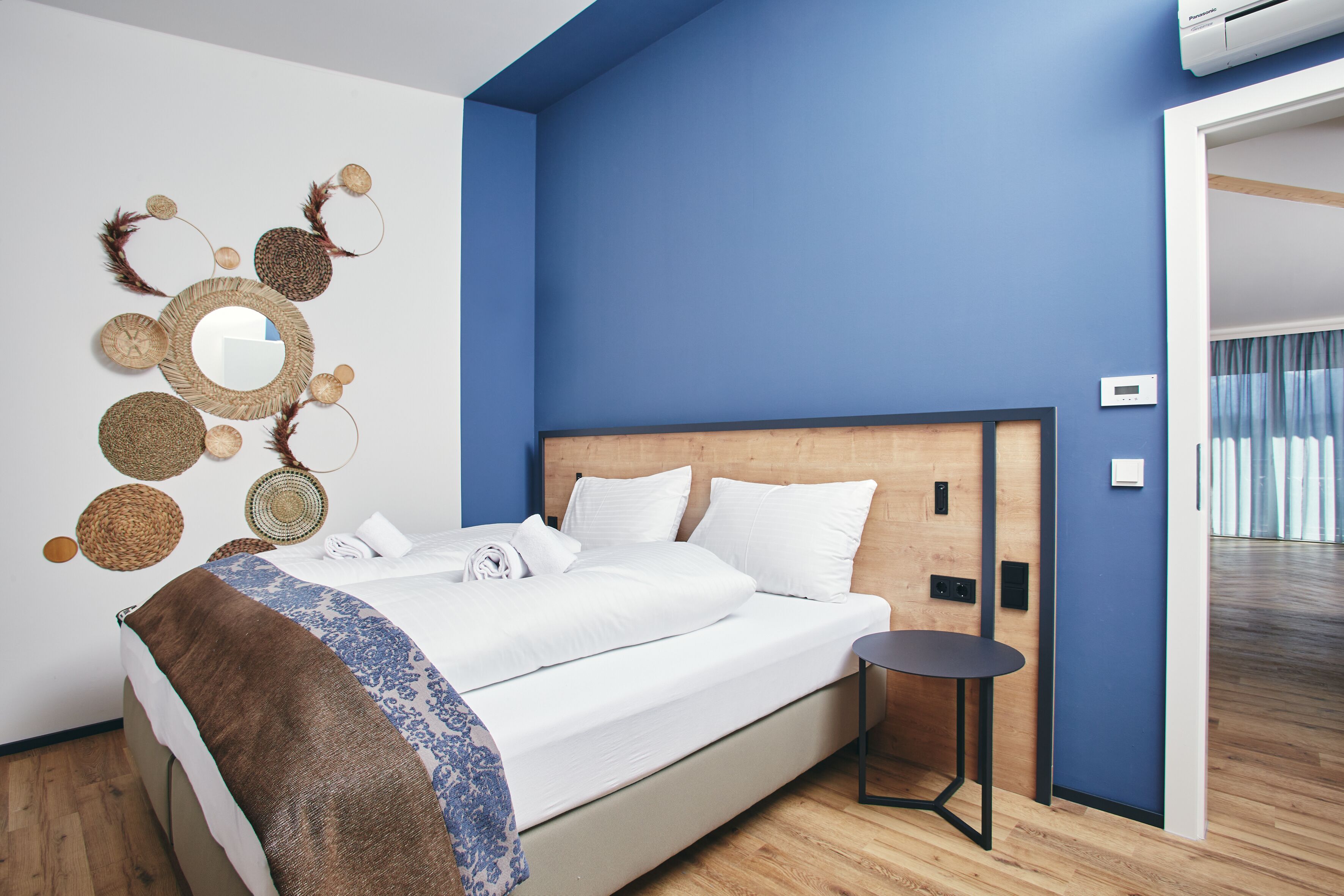 A modern hotel room with a large bed, a small table, and a wall-mounted mirror.
