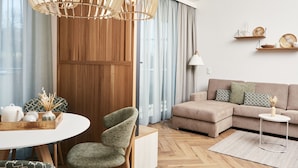 Ein modernes Wohnzimmer mit einem Holzesstisch, einem grünen Polsterstuhl, einem beigefarbenen Sofa und einem weißen Beistelltisch.