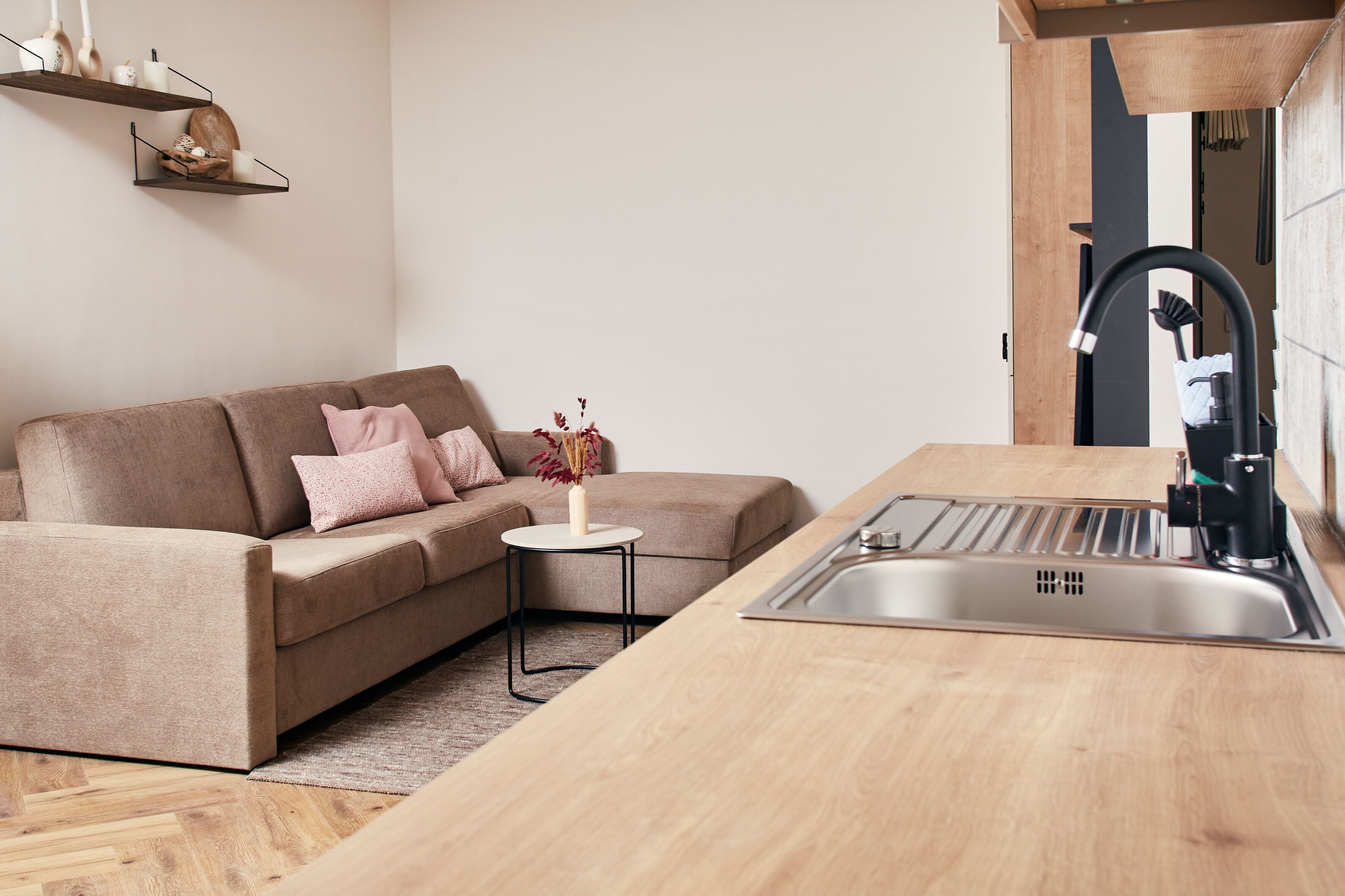 Una cucina moderna con lavello incassato, piano di lavoro in legno e divano beige con cuscini rosa.