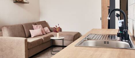 A modern kitchen with a built-in sink, a wooden countertop, and a beige sofa with pink cushions.