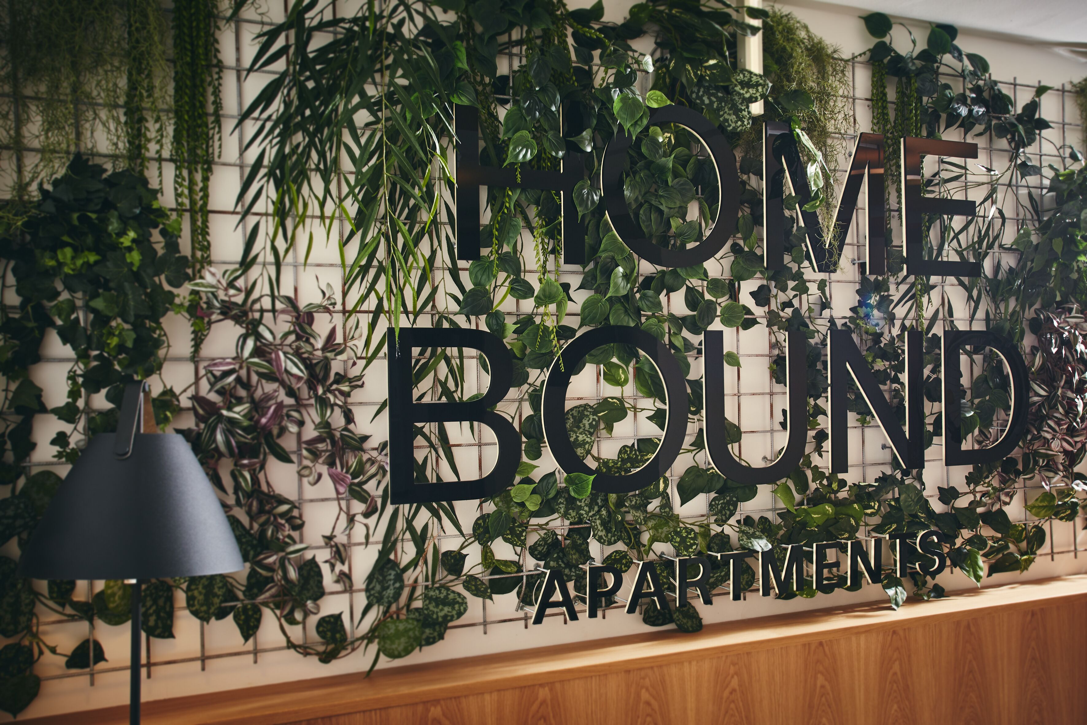 A wall with the text "HOME BOUND APARTMENTS" surrounded by lush green plants.