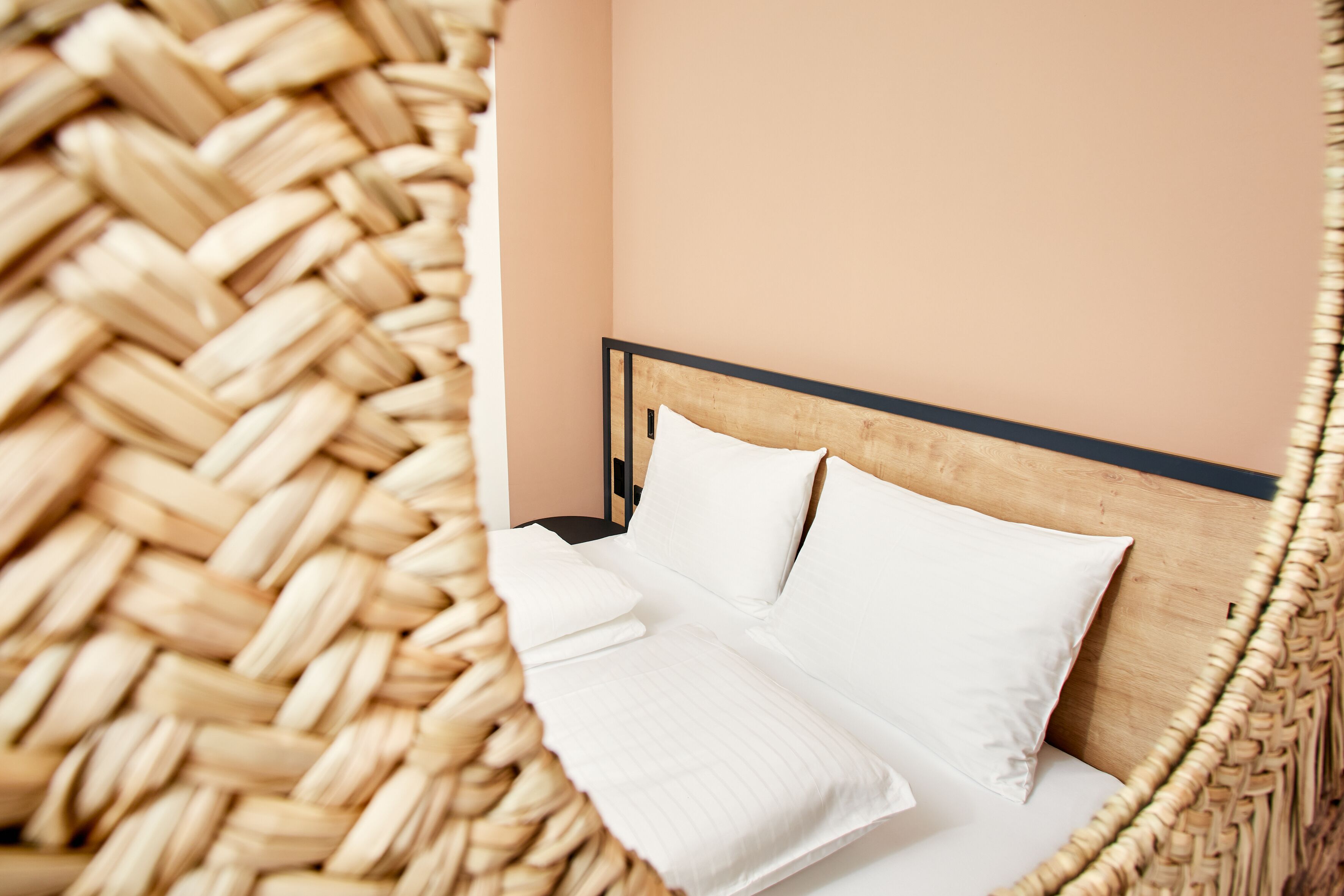A bed with white linens and a wooden headboard in a room with a woven basket on the floor.