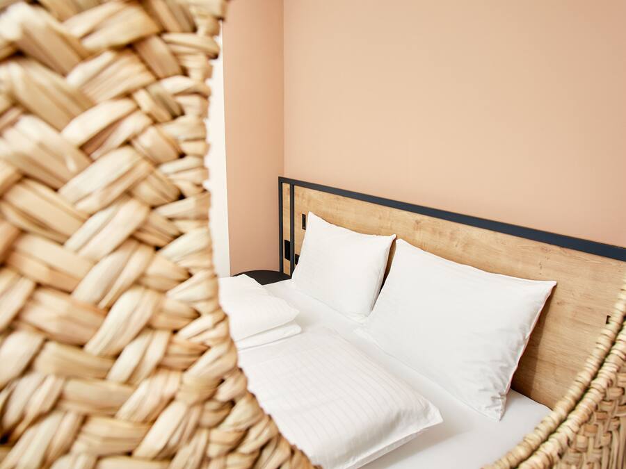 A bed with white linens and a wooden headboard in a room with a woven basket on the floor.