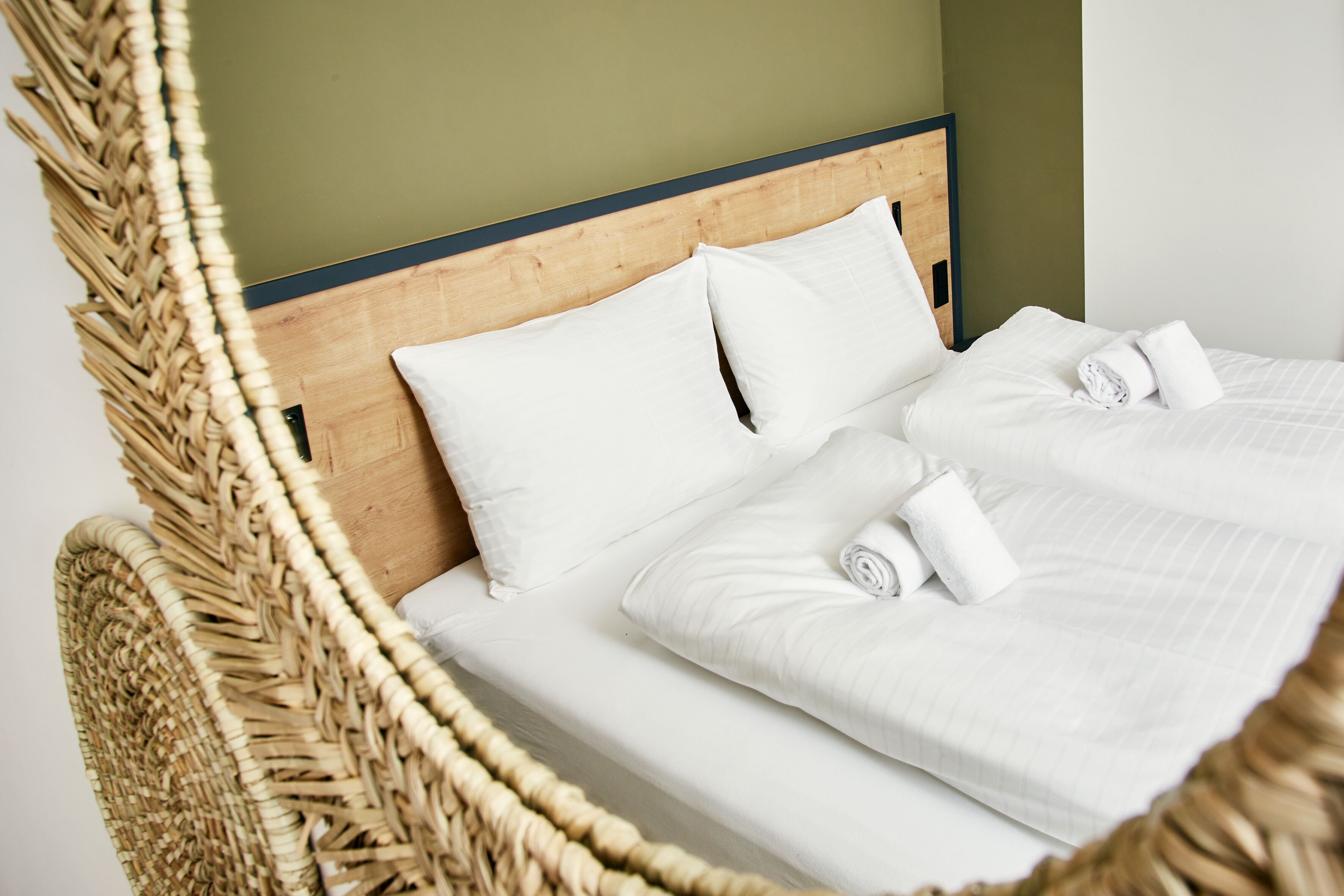 A bed with white linens and pillows, a wooden headboard, and a woven chair.
