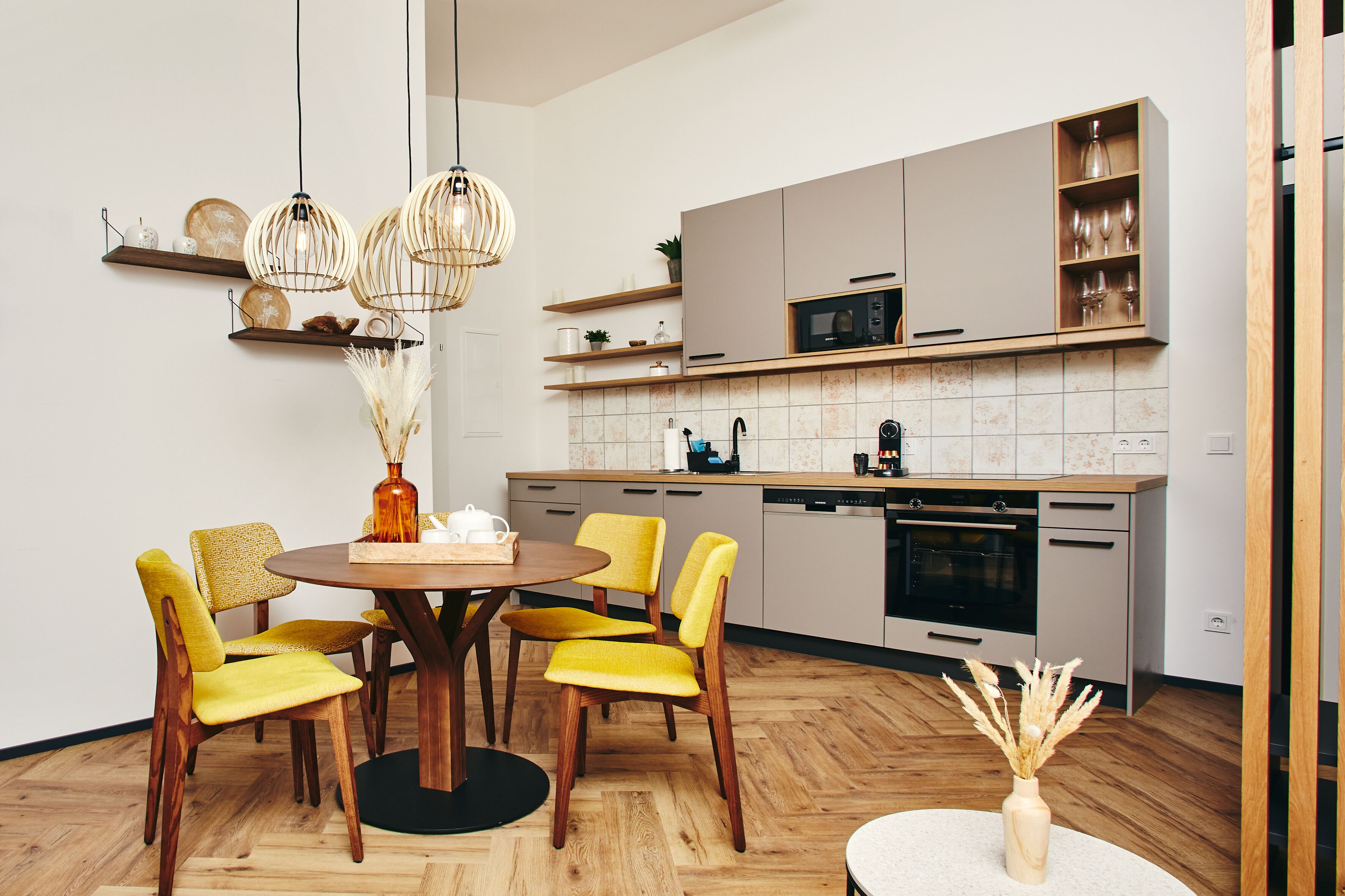 A modern kitchen with wooden cabinets, a microwave, and a dining area with yellow chairs and a round table.