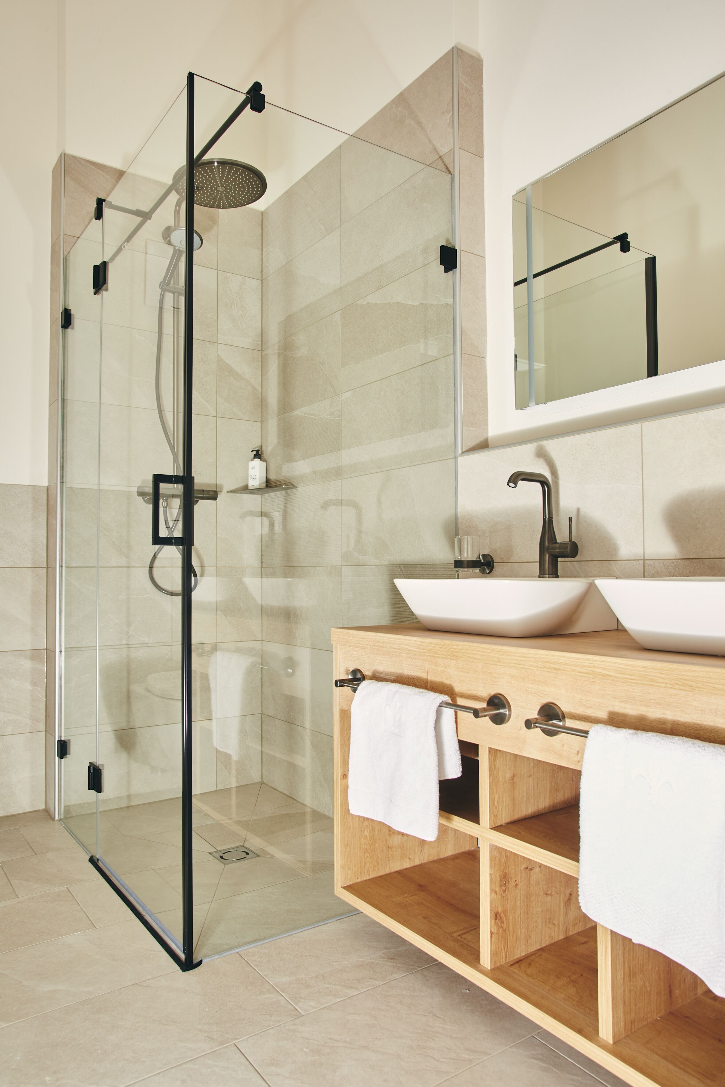 A modern bathroom with a glass-enclosed shower, two sinks, and a wooden vanity.