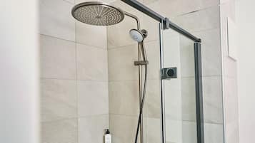 Ducha con cerramiento de vidrio, cabezal de ducha de mano y panel de control en la pared.