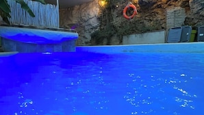 Una piscina con un tono azul, un flotador en la pared y una estructura de madera con techo.