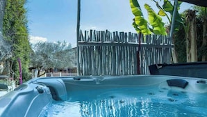 Un jacuzzi con cerca de madera y plantas de plátano al fondo.
