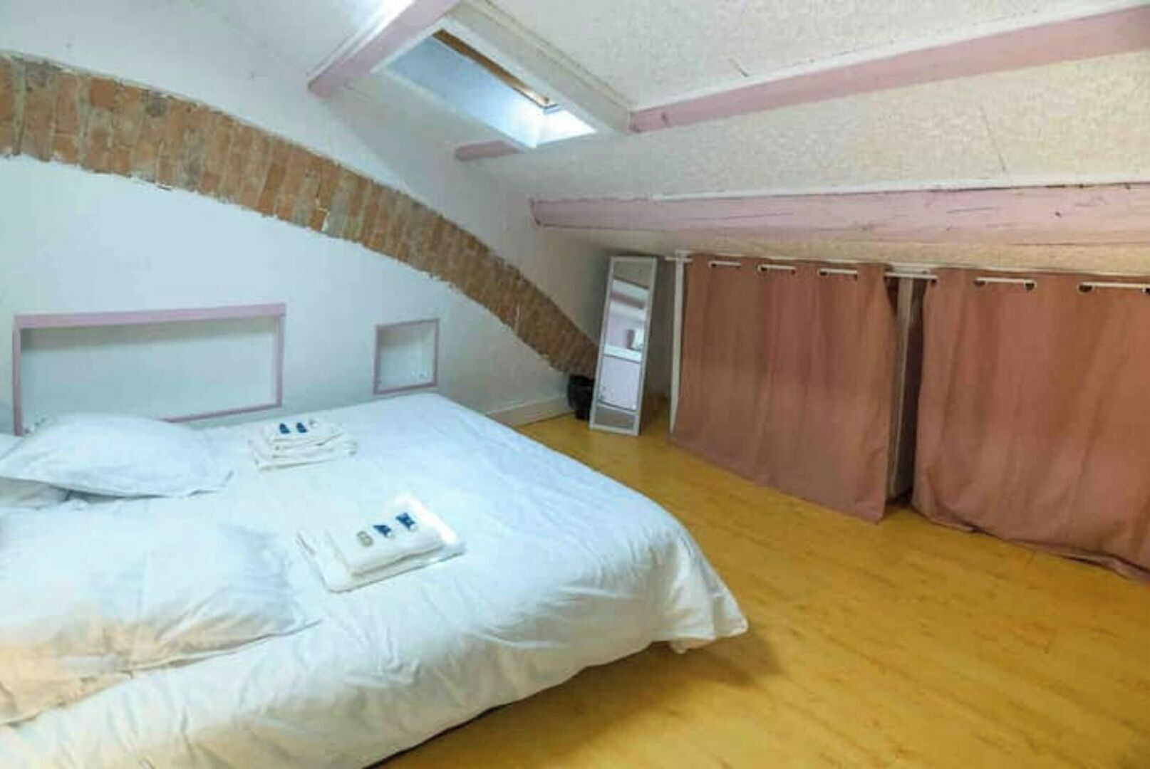 Ein Schlafzimmer mit schrägen Wänden, einem Bett mit weißen Leinen, Holzboden und einem Fenster.