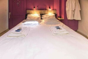 A double bed with white linens, two folded towels, and a wooden headboard.