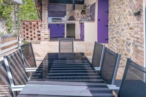 An outdoor dining area with a black table and chairs, a brick wall, and a purple door in the background.