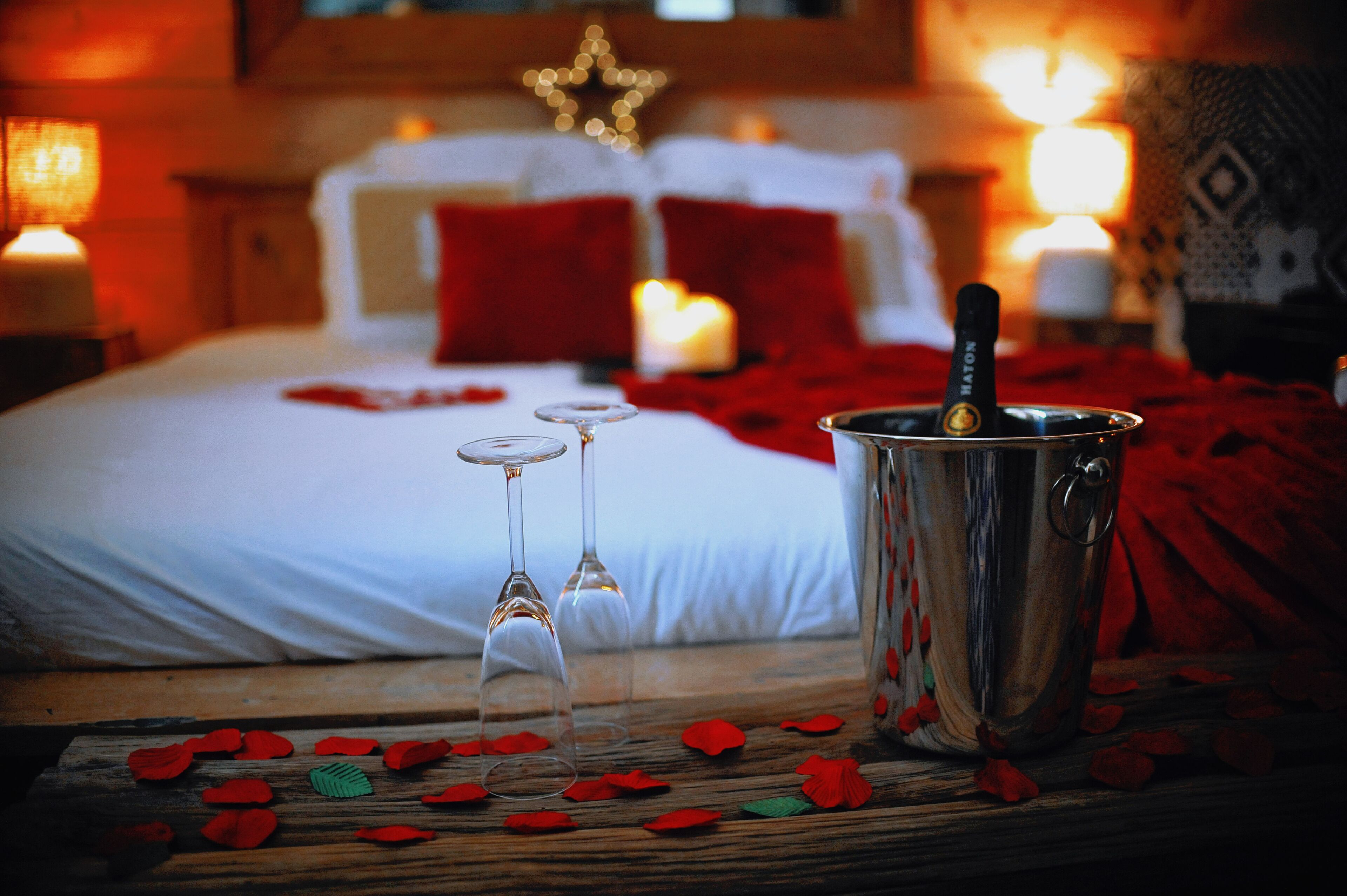 Uma cama com pétalas de rosa, duas taças de vinho e uma garrafa de champanhe sobre uma mesa de madeira.