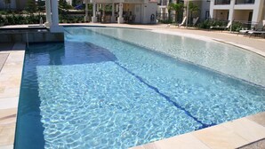 Una piscina rectangular con agua cristalina, rodeada por una solana con baldosas y un área de estar cubierta con sillas.