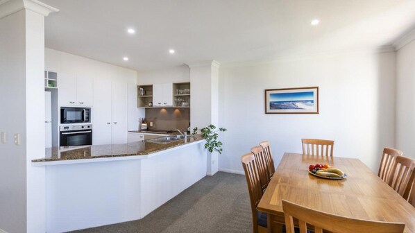 Una cocina moderna con armarios blancos, encimera de granito y un comedor con mesa y sillas de madera.