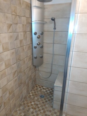 Une douche équipée d’un pommeau de douche à main et d’un panneau de commande fixé au mur.
