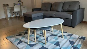 Uma sala de estar com um sofá cinzento, uma mesa de centro branca e um tapete estampado.