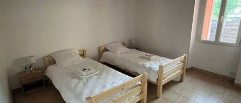 A small, clean room with two wooden beds, a nightstand, and a window with blinds.