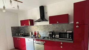 Uma cozinha moderna com armários vermelhos, lava-louças, micro-ondas e cafeteira.