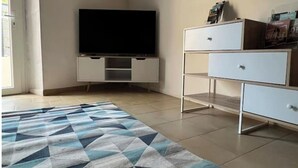 Quarto com televisão de tela plana sobre um móvel branco, tapete estampado e estante branca com gavetas.