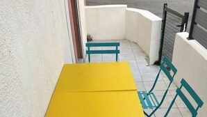 Uma mesa amarela com cadeiras verde-água num pátio com ladrilhos.