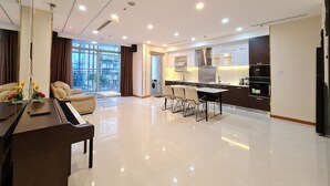 A modern living room with a piano, a dining area, and a kitchen with dark cabinets and a marble countertop.