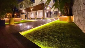 A modern building with a well-lit entrance, paved pathways, and a grassy area. - Sky Taj Villa 5 BHK (Igatpuri)
