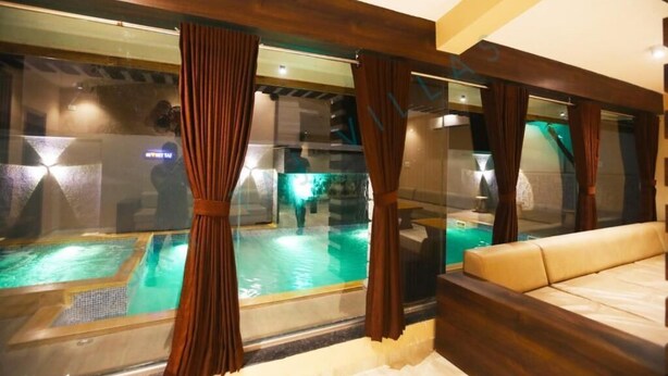 A room with a view of an indoor swimming pool, a sofa, and a ceiling with a logo. - Sky Taj Villa 5 BHK (Igatpuri)