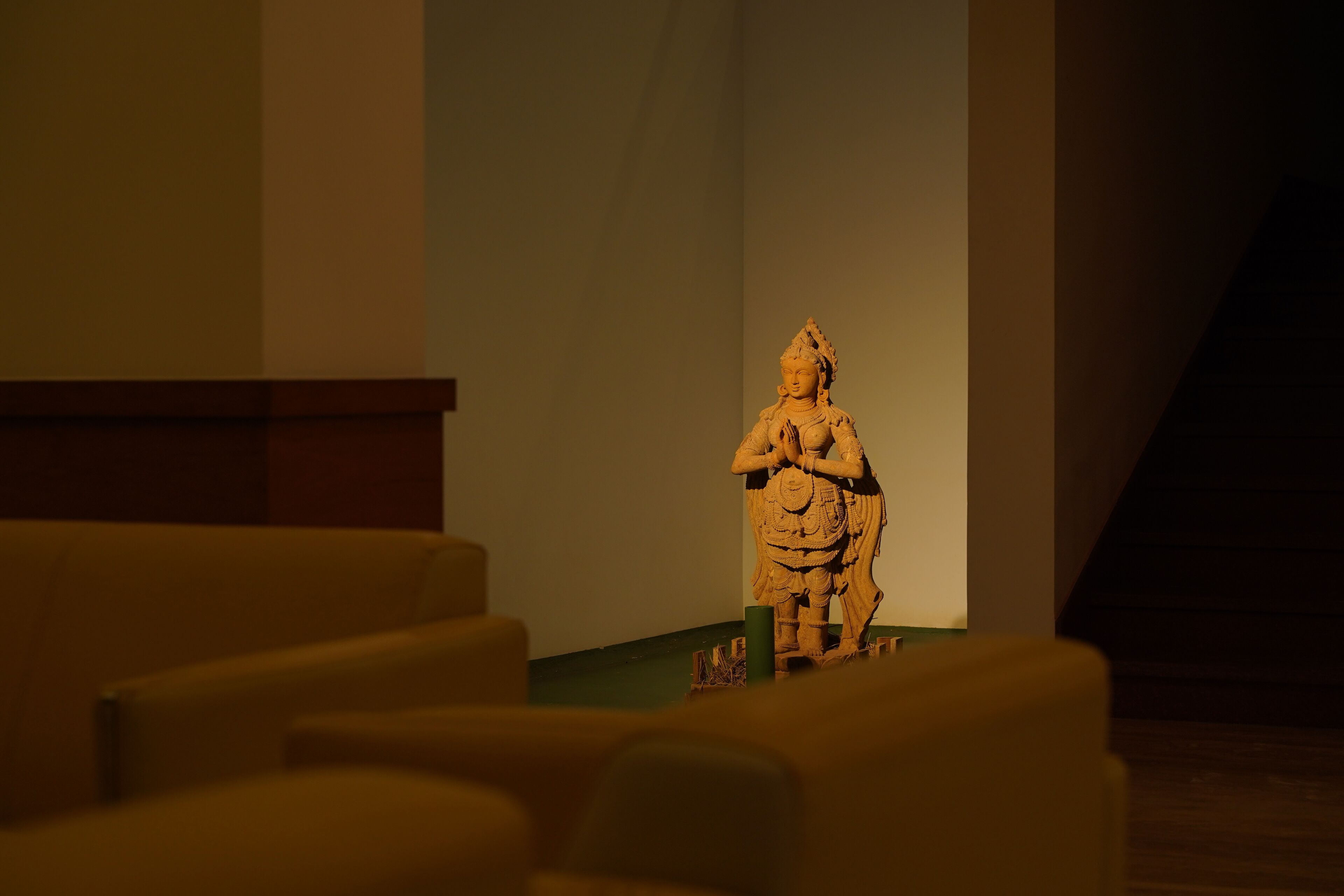 Una estatua en una habitación tenuemente iluminada, con una escalera al fondo.