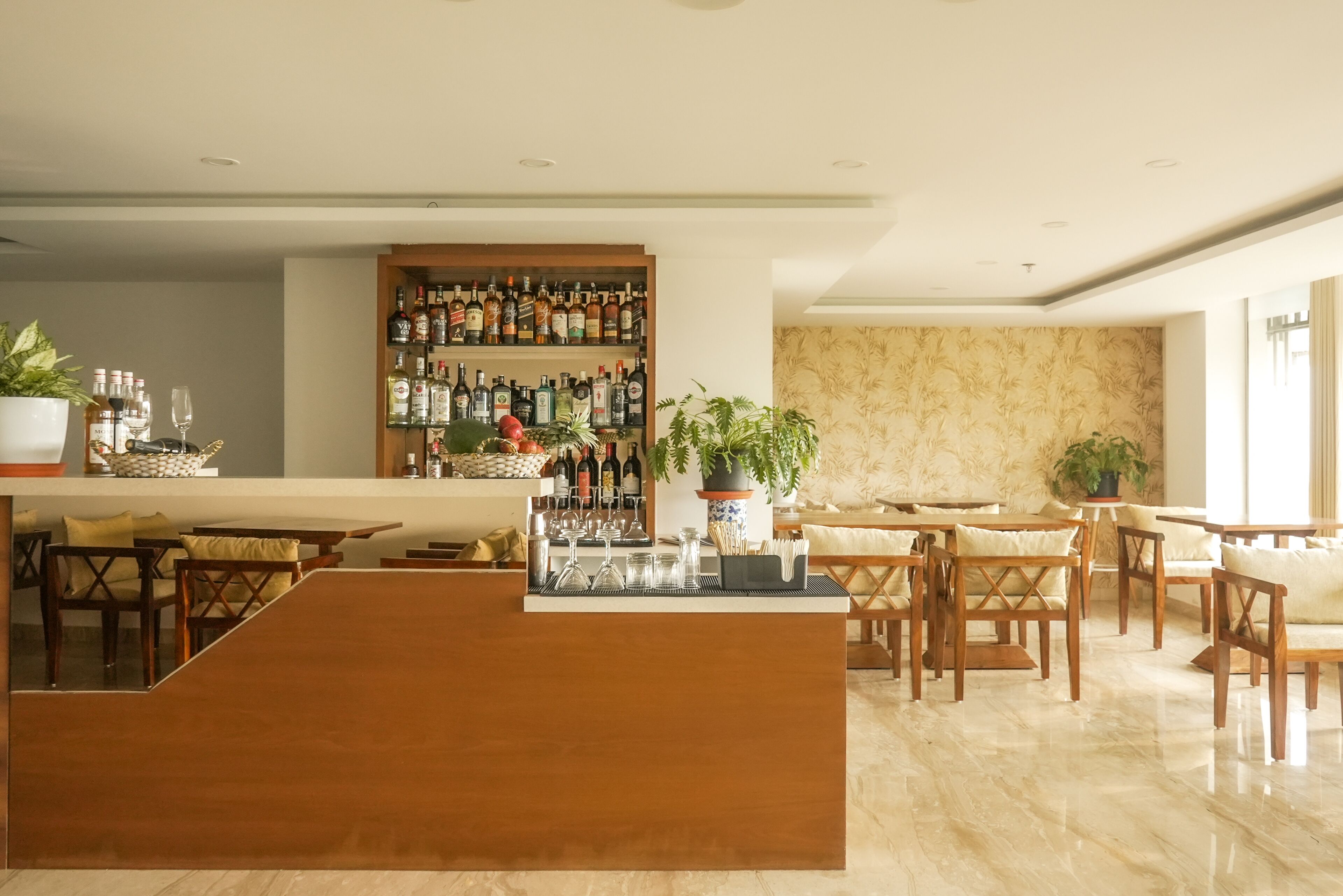 Una zona de bar con mostrador de madera, varios arreglos de asientos y una pared llena de botellas de licor.