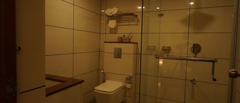 A small, modern bathroom with a toilet, a glass shower enclosure, and a towel rack.
