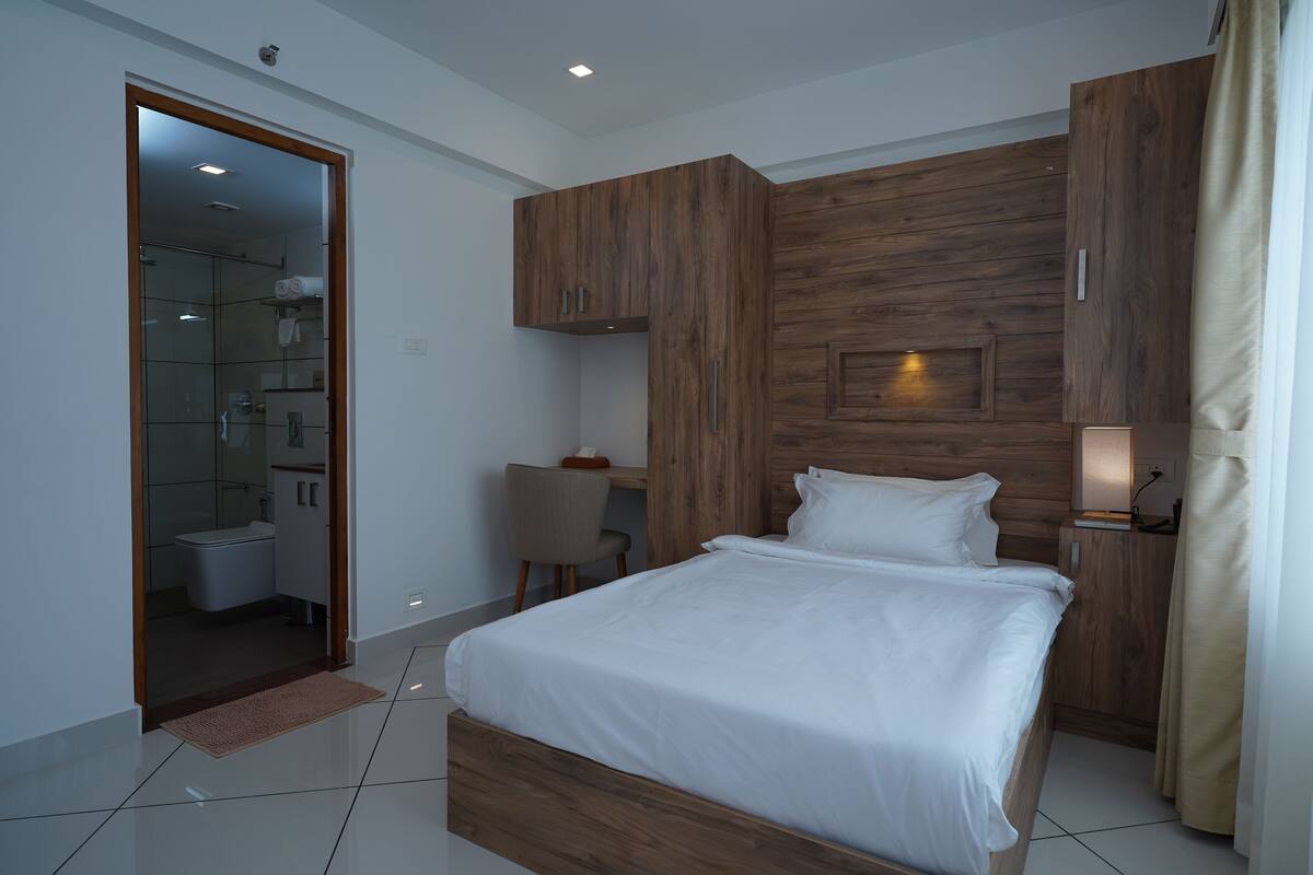 A modern bedroom with a wooden headboard, a bedside table with a lamp, and a glass shower enclosure.