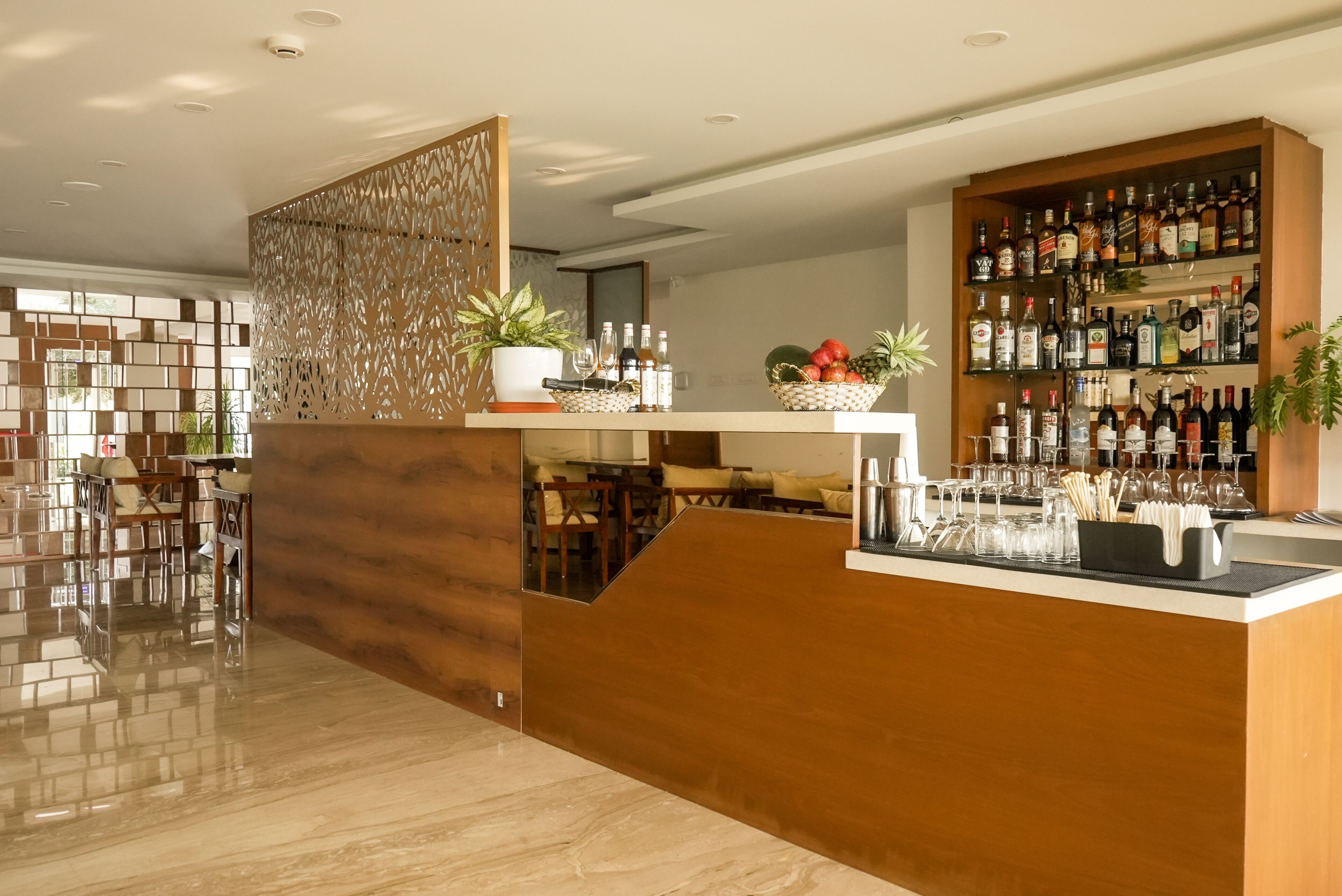 A modern bar area with a wooden counter, shelves of liquor bottles, and a seating area with chairs and a table.