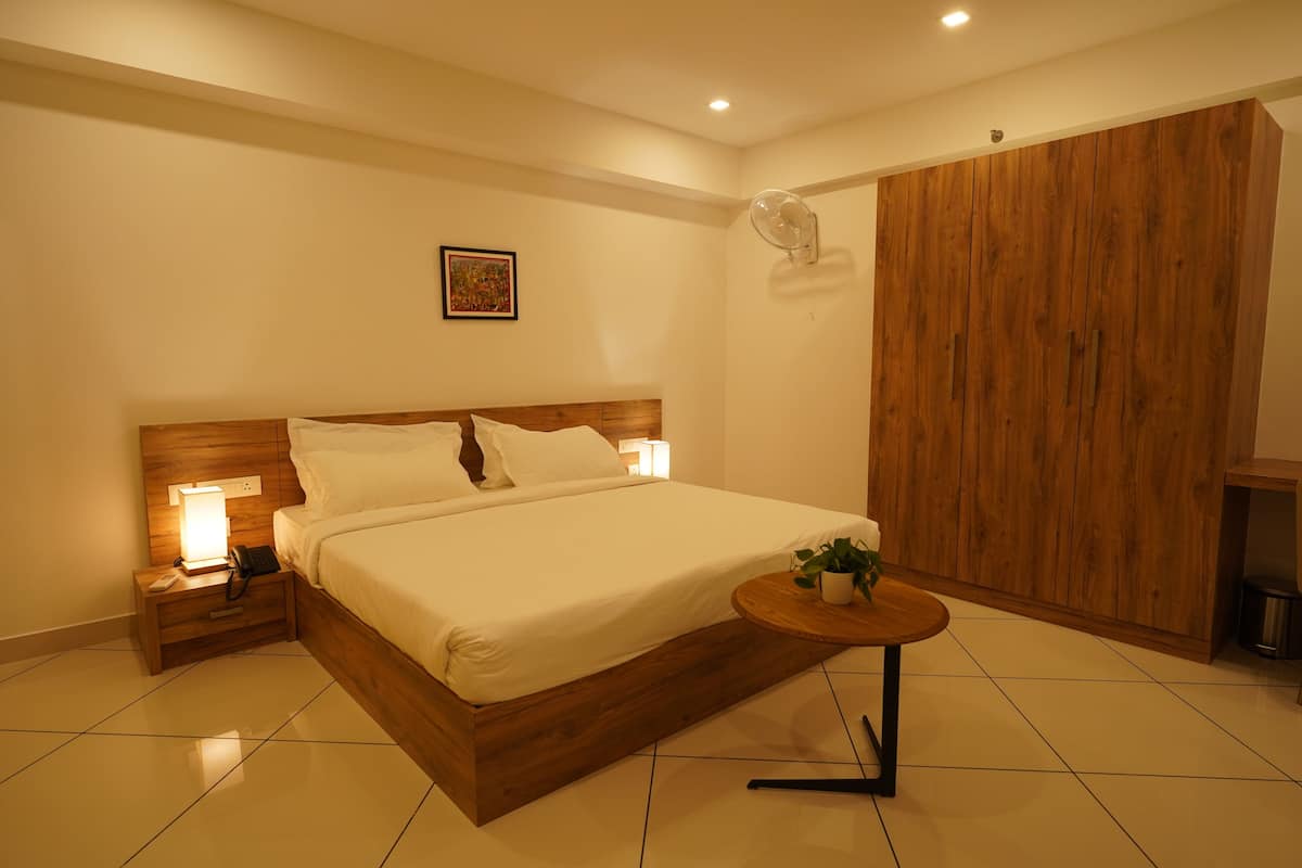 A hotel room with a wooden bed, bedside lamps, a small round table with a plant, and a wooden wardrobe.